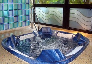 Un bain à remous doté d’un escalier en métal, entouré d’un sol carrelé et de murs en verre aux motifs ondulés.