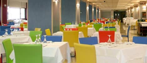 Un espace repas comprenant plusieurs tables et chaises, une porte de sortie bien visible et un plafond doté d’un éclairage encastré.