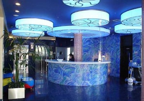 A reception area with a central counter, large blue patterned walls, and a modern design. - Magic INN (Oropesa del Mar)