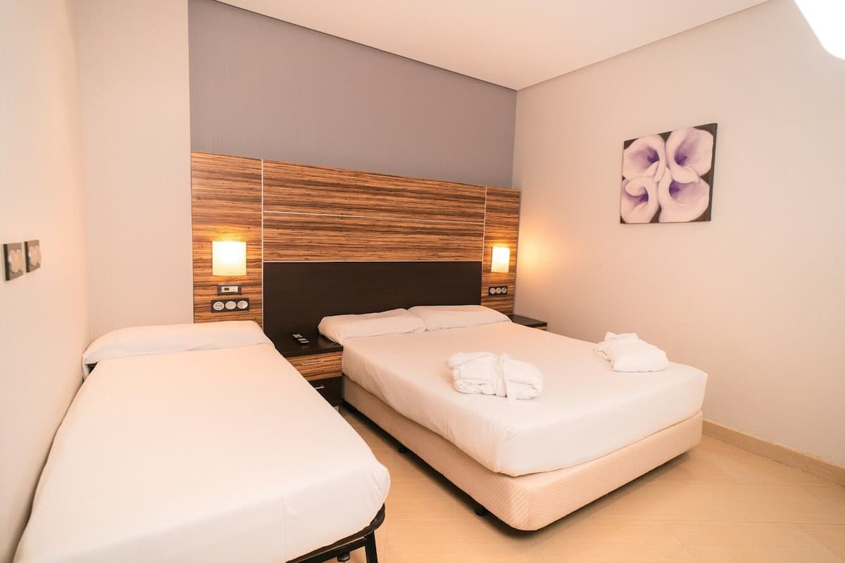 A hotel room with two beds, a wooden headboard, bedside lamps, and a wall-mounted artwork.