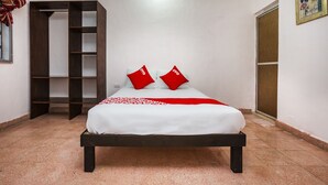 A bedroom with a bed, two red pillows, a white bedspread, a wooden wardrobe, and a tiled floor. - Casa Cuevas & Amaro (Mérida)