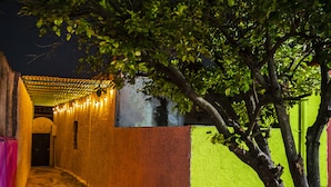A narrow alleyway with a tree and string lights, leading to a building with a green wall and a pink structure. - Casa Cuevas & Amaro (Mérida)