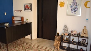 A room with a dark wooden desk, a patterned rug, a shelf with statues and decorative items, and a door with a dark frame. - Casa Cuevas & Amaro (Mérida)