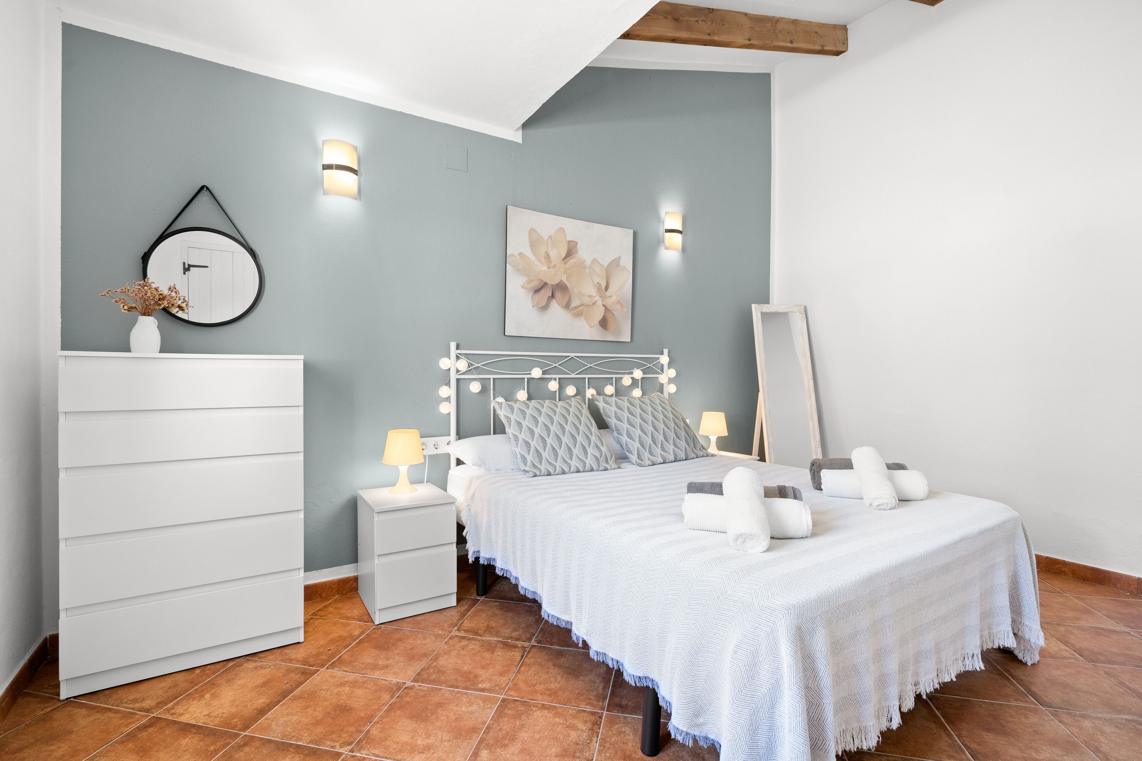 A bedroom with a bed, bedside tables, a dresser, wall-mounted lights, and a mirror.