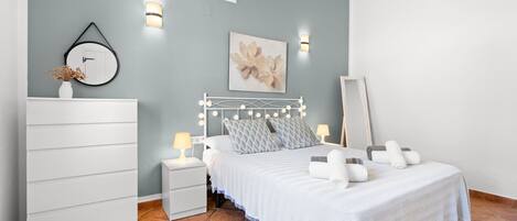 A bedroom with a bed, bedside tables, a dresser, wall-mounted lights, and a mirror.
