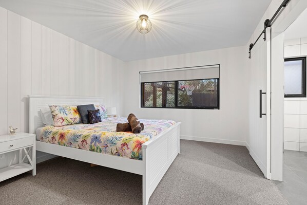 A bedroom with a bed, a nightstand, a window with a view, and a door.