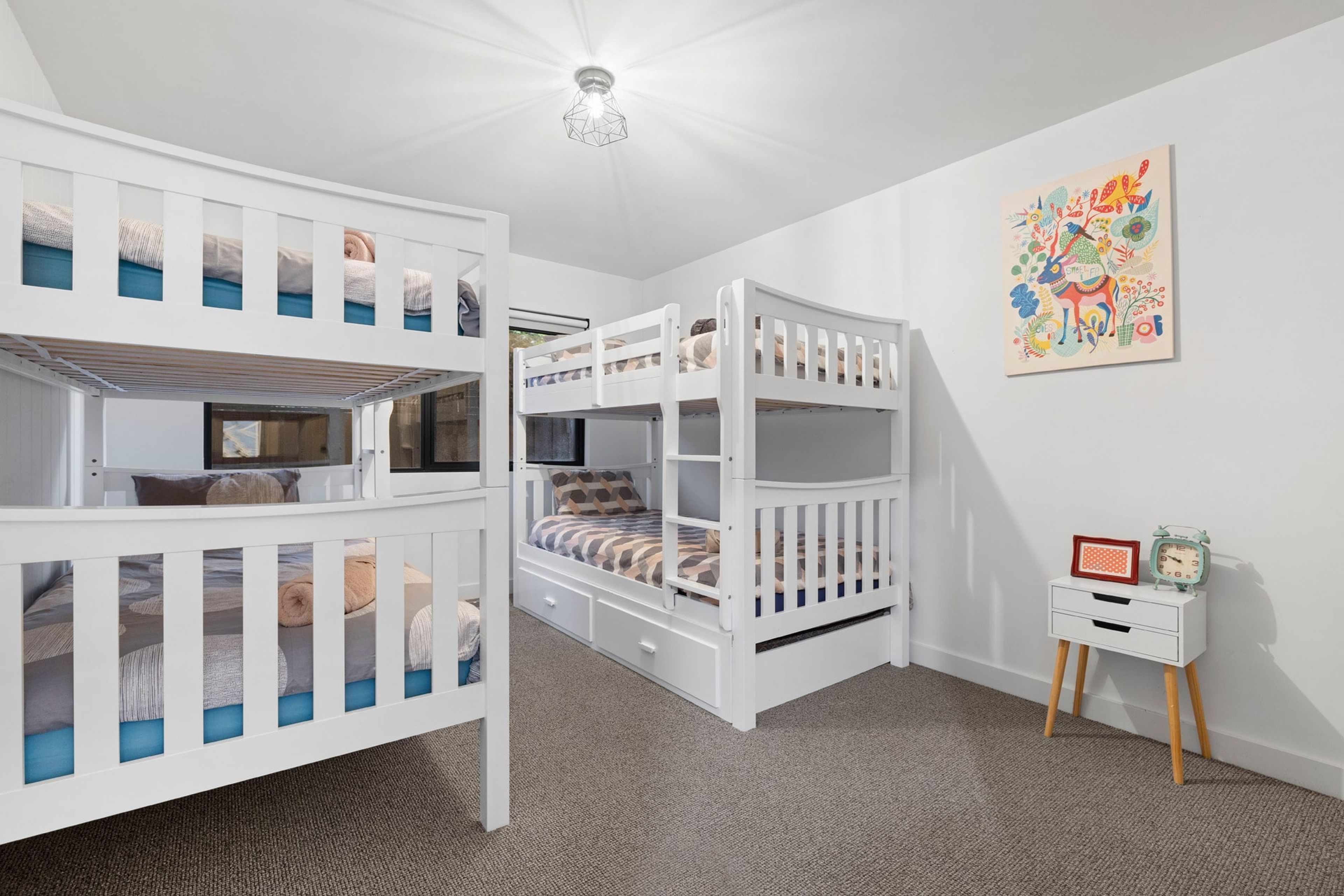 A room with bunk beds, a small bedside table with an alarm clock, and a colorful wall decoration.