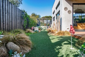 Um caminho leva a um edifício de design moderno, com uma cerca de madeira de um lado e diversas plantas e pedras ao longo do percurso.