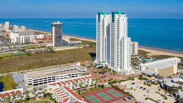 Een hoog hotel met meerdere verdiepingen, een parkeergarage en uitzicht op het strand.