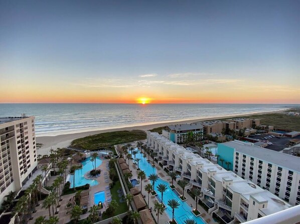Un resort con varias piscinas, acceso a la playa y vista al atardecer.
