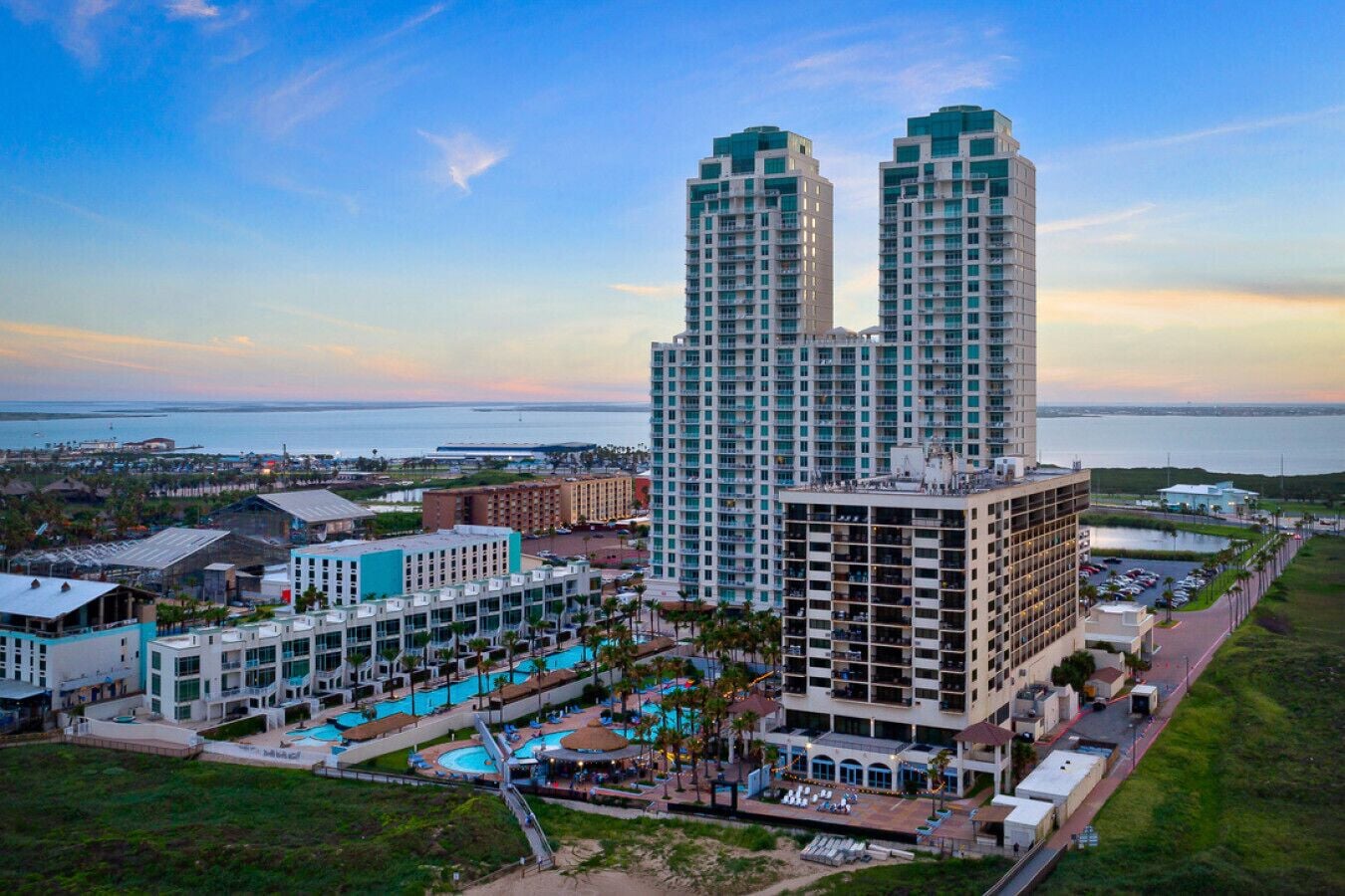 A high-rise hotel with multiple balconies, a swimming pool area, and a view of the ocean.