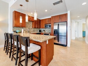 A modern kitchen with a central island, bar stools, stainless steel appliances, and pendant lighting.