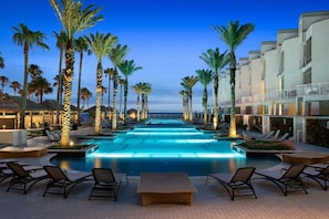 A swimming pool with lounge chairs and palm trees, surrounded by hotel buildings.