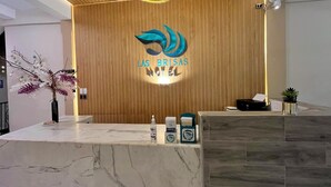 Zona de recepción de hotel con pared de paneles de madera, un mostrador de recepción de mármol y un logotipo sobre el mostrador.