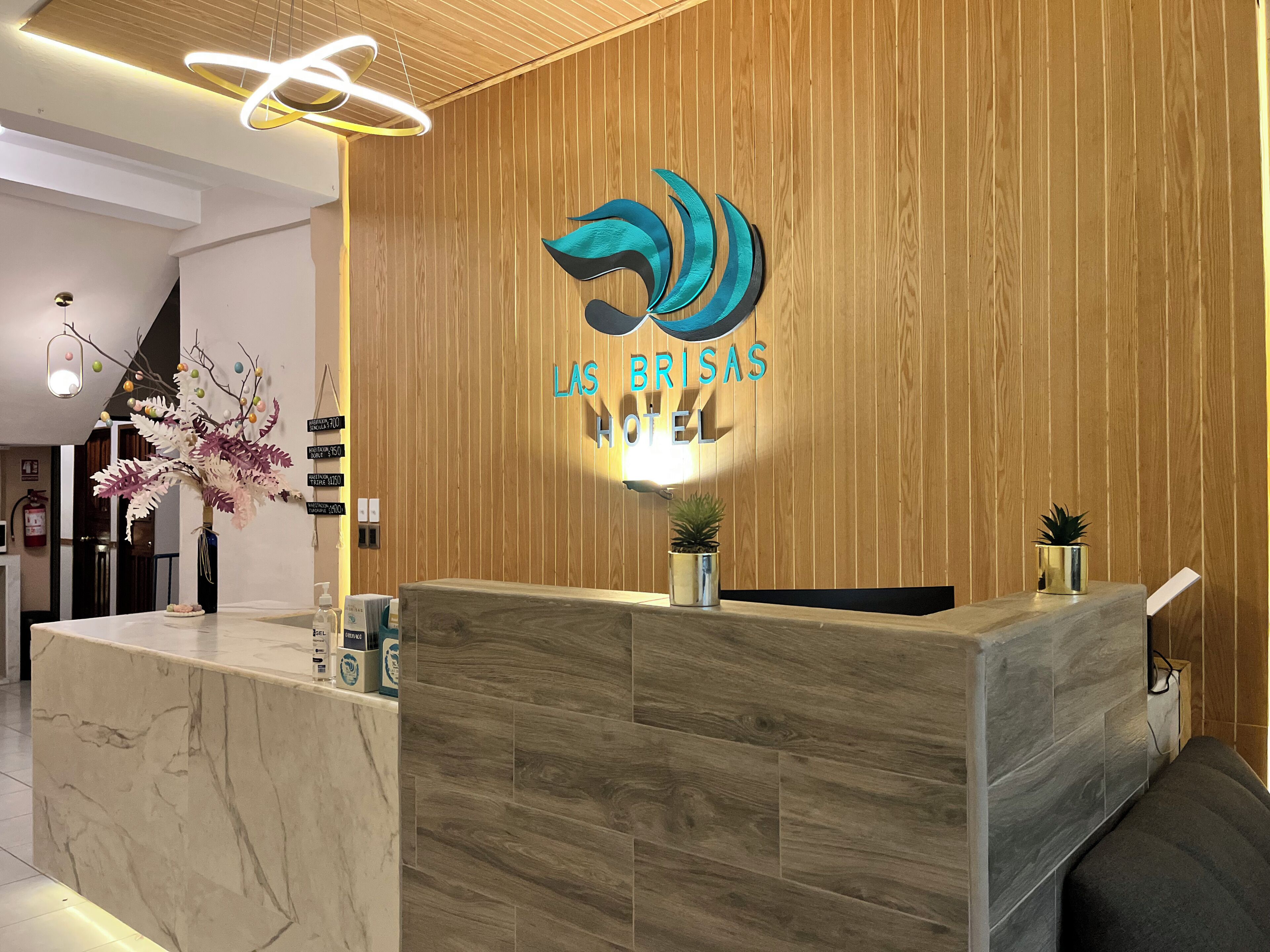 A hotel reception desk with a wooden panel wall, a logo above the reception area, and a modern light fixture.