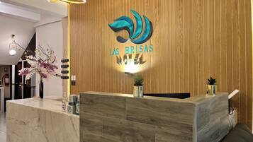 A hotel reception desk with a wooden panel wall, a logo above the reception area, and a modern light fixture.
