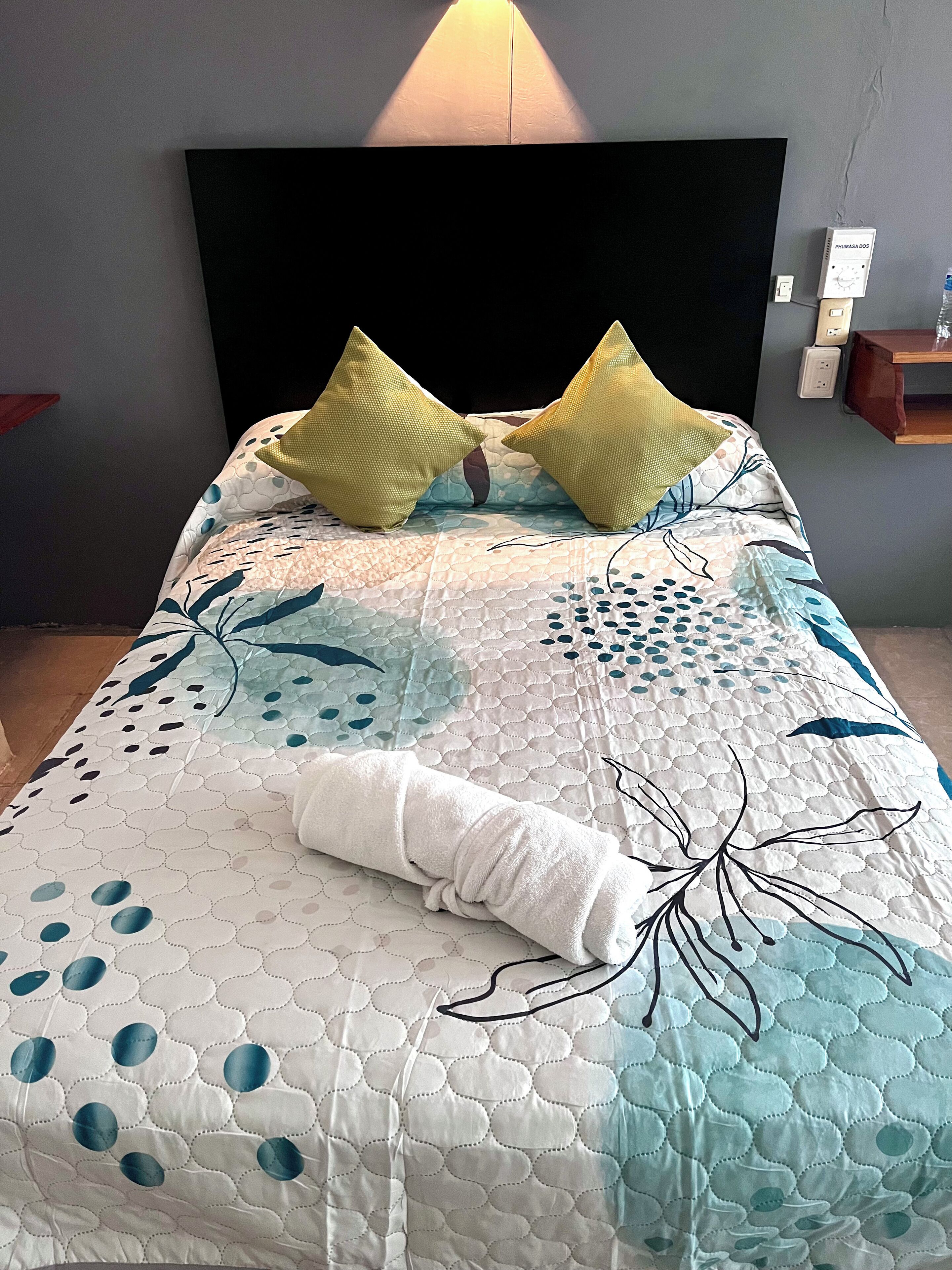 Una cama con cabecera acolchada, dos almohadas y una toalla enrollada.