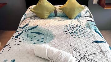 Una cama con cabecera acolchada, dos almohadas y una toalla enrollada.