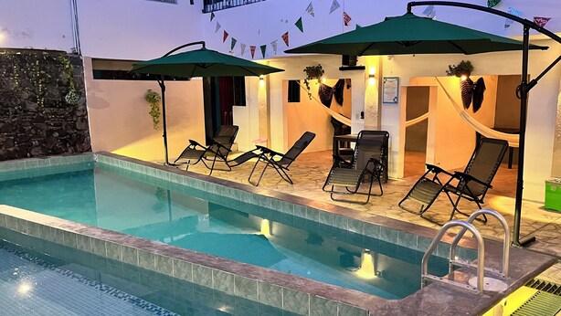 Una piscina con sillas de descanso y sombrillas, rodeada de muros de piedra y un suelo de baldosas.