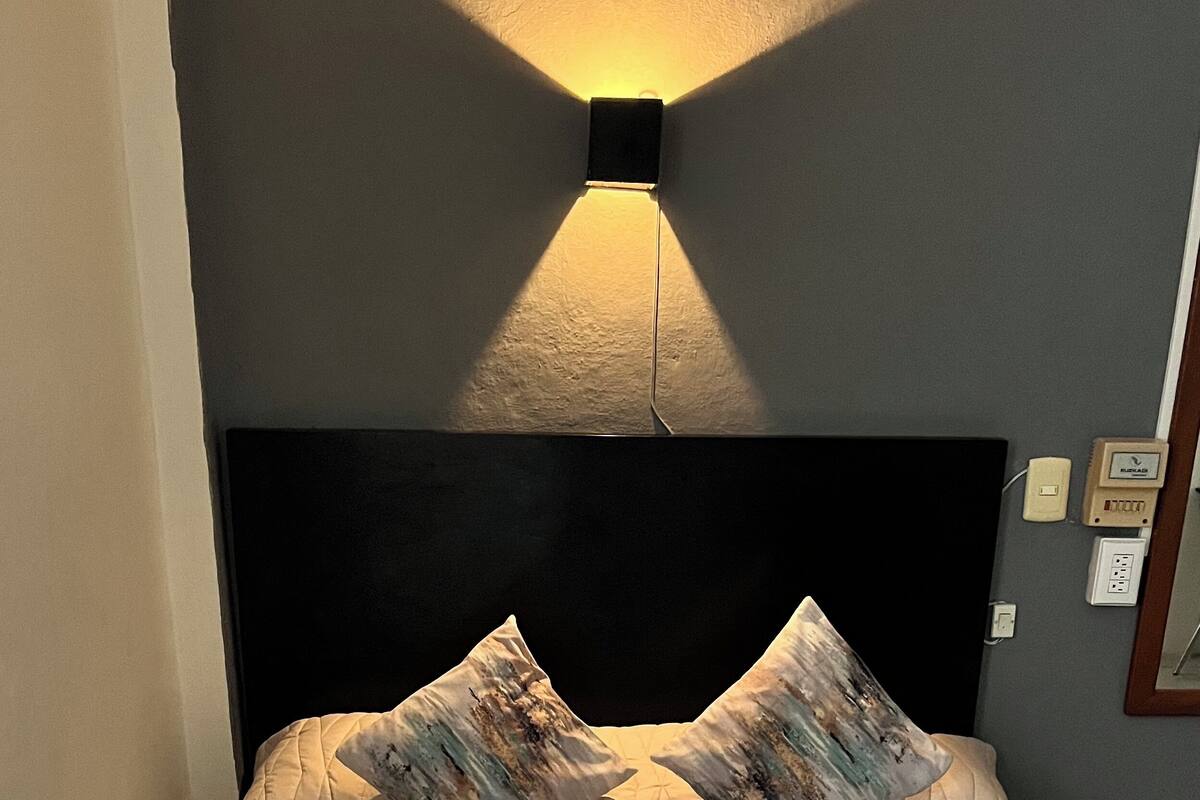 A neatly made bed with a quilted beige bedspread, two patterned pillows, and a folded white towel on the bed.