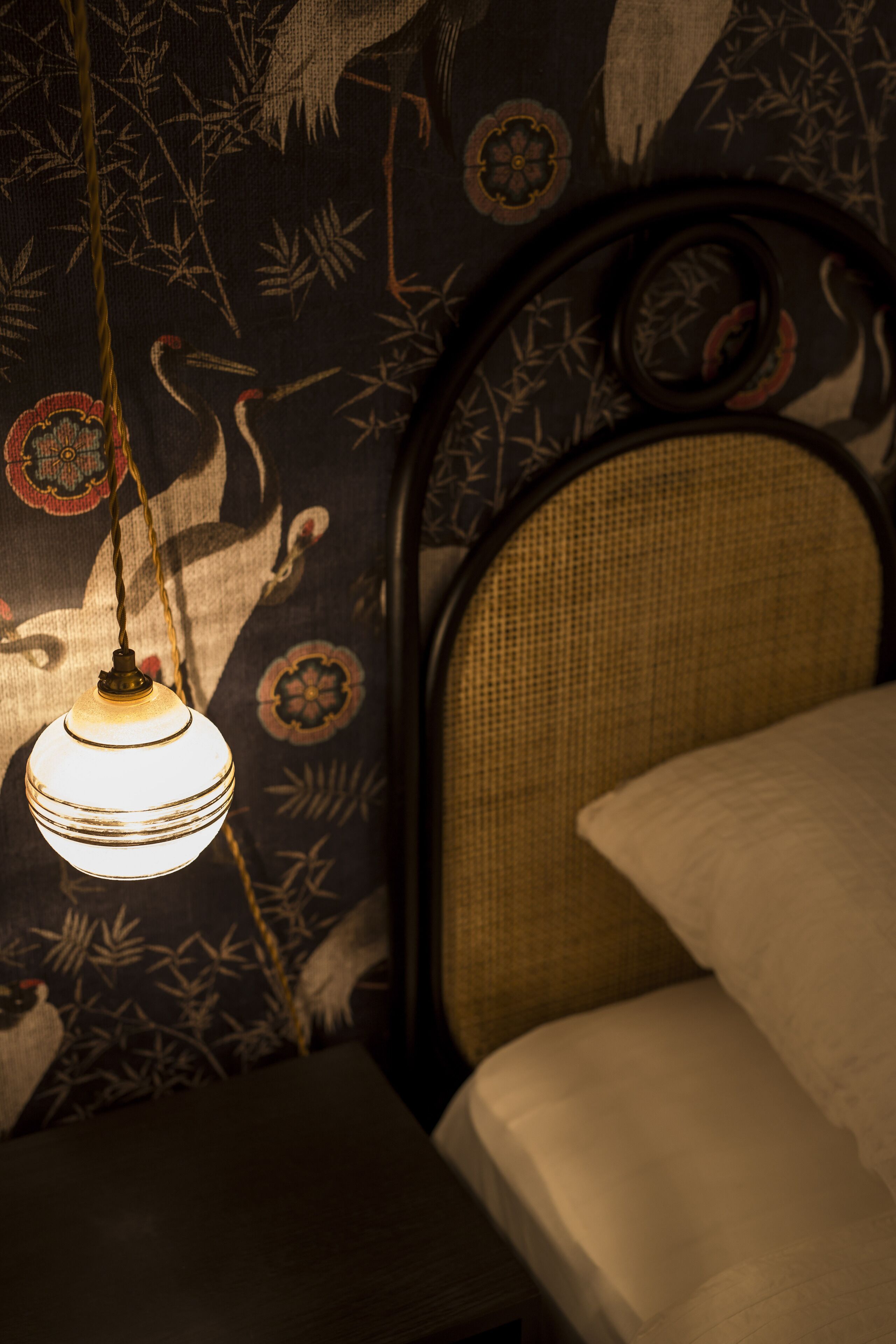 Una cama con cabecera trenzada, una lámpara colgante y una pared con estampado floral.