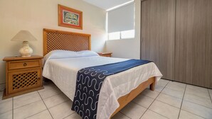 Quarto com cama de madeira, mesa de cabeceira com abajur, quadro na parede e janela com persianas.