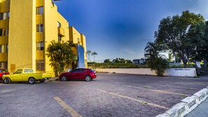 Uma área de estacionamento com um edifício amarelo, um carro vermelho e um caminhão amarelo.