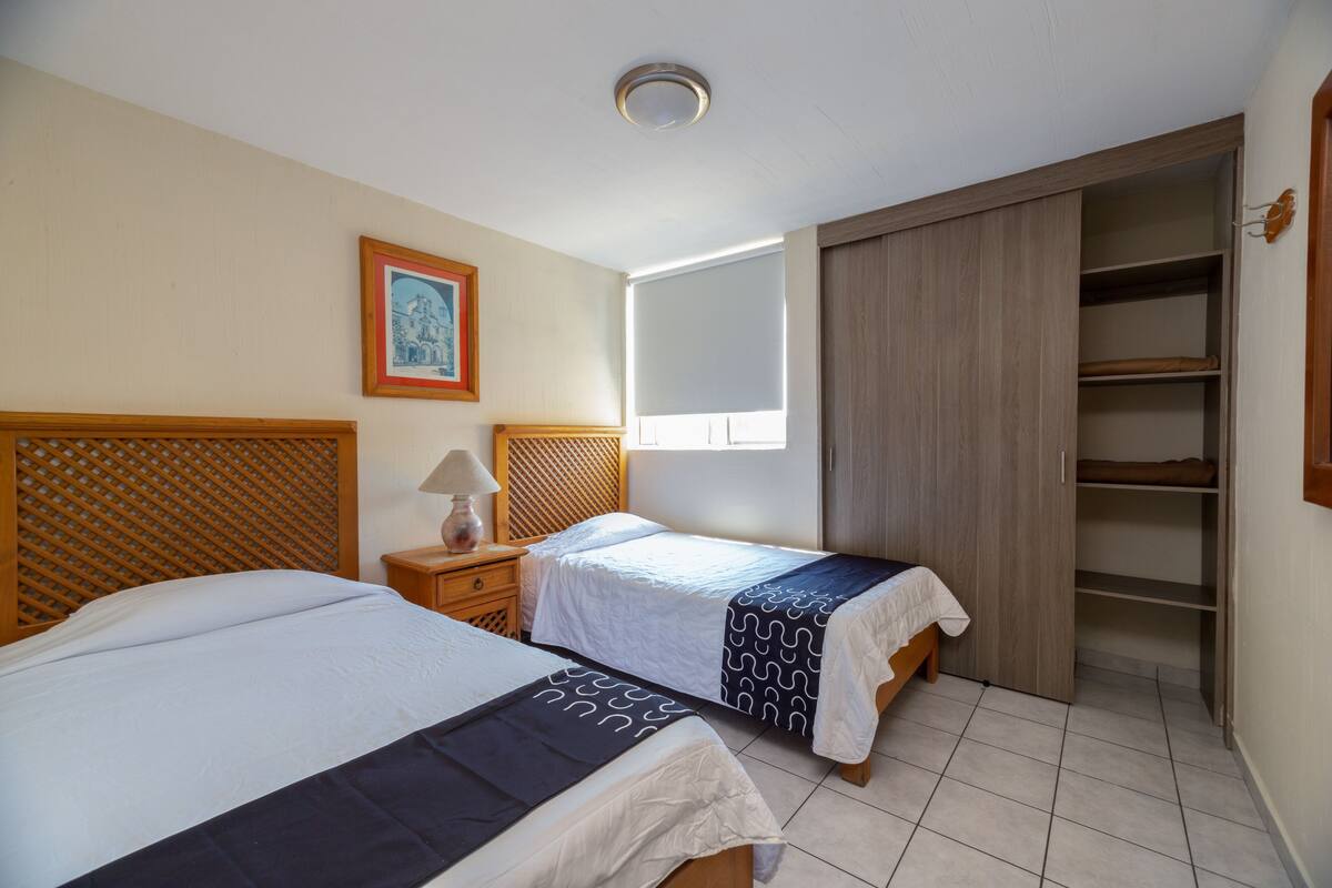A bedroom with two beds, a wooden headboard, a nightstand with a lamp, a wardrobe, and a framed picture on the wall.
