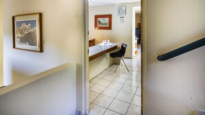 Um corredor com um quadro na parede, uma mesa com uma cadeira e um chão de azulejos.