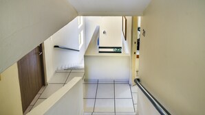 Uma escadaria estreita com corrimão, uma porta de madeira e uma pequena janela.