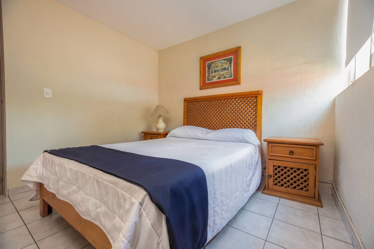 A neatly made bed with a wooden headboard, a bedside table with a lamp, and a framed picture on the wall.