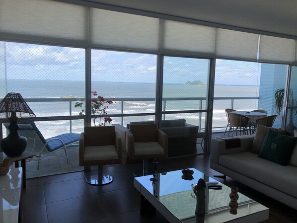 A spacious living area with a large balcony overlooking the ocean, furnished with a sofa, chairs, and a coffee table.