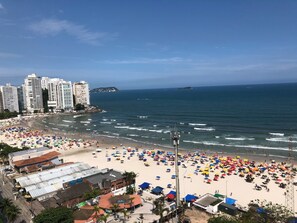 Una playa con numerosos sombrillas y gente, una costa con edificios y un cielo despejado.