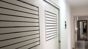 Un pasillo con una puerta cerrada, un respiradero en la pared y una lámpara.