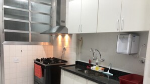 Cocina compacta con gabinetes blancos, estufa negra, campana de acero inoxidable, un lavabo con grifo y dispensador de agua.
