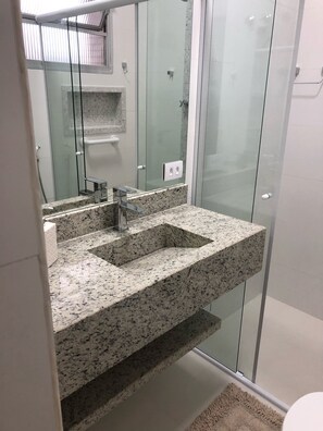 A modern bathroom with a granite sink, glass shower enclosure, and a large mirror.