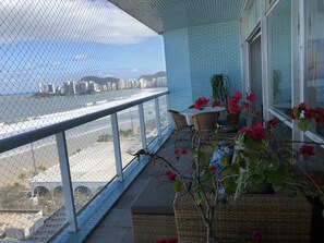 A balcony with a view of the beach and cityscape, wicker furniture, and potted plants.