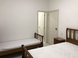 A bedroom with two single beds, a small bedside table, and a door leading to another room.
