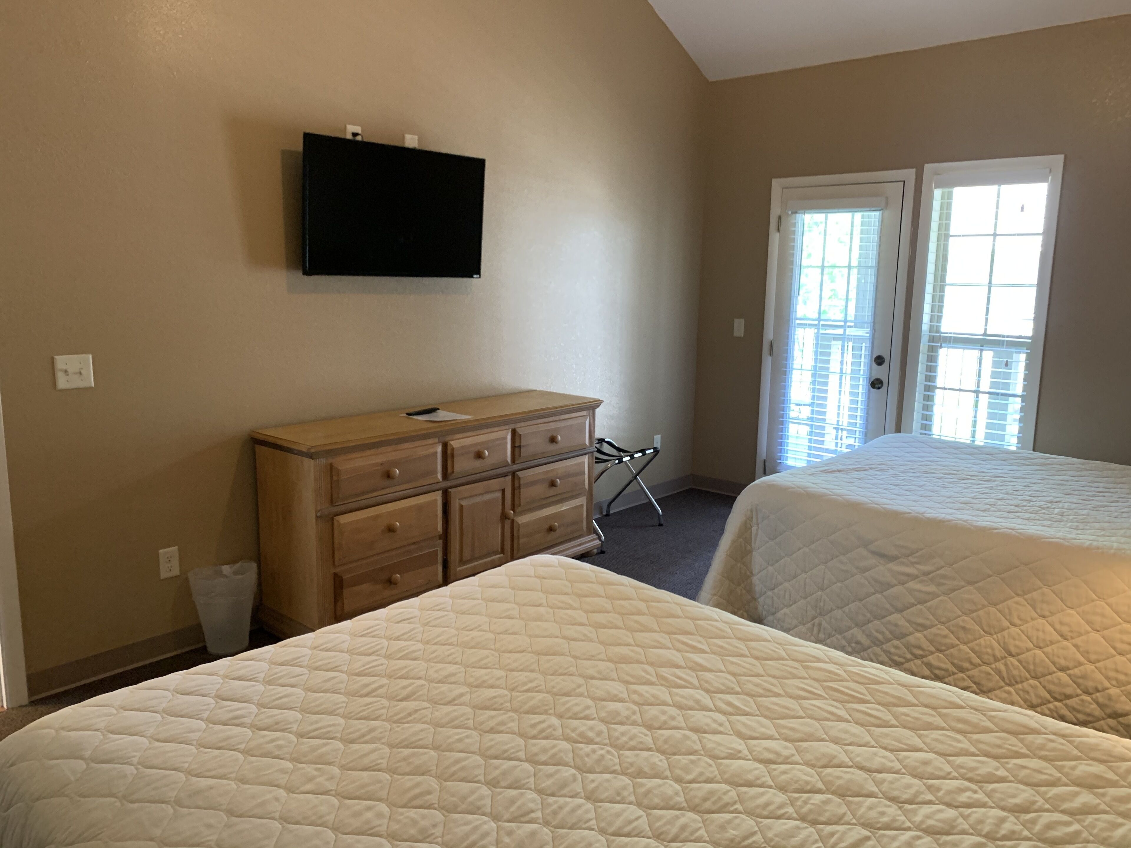 A hotel room with two beds, a dresser, a TV mounted on the wall, and a door leading outside.