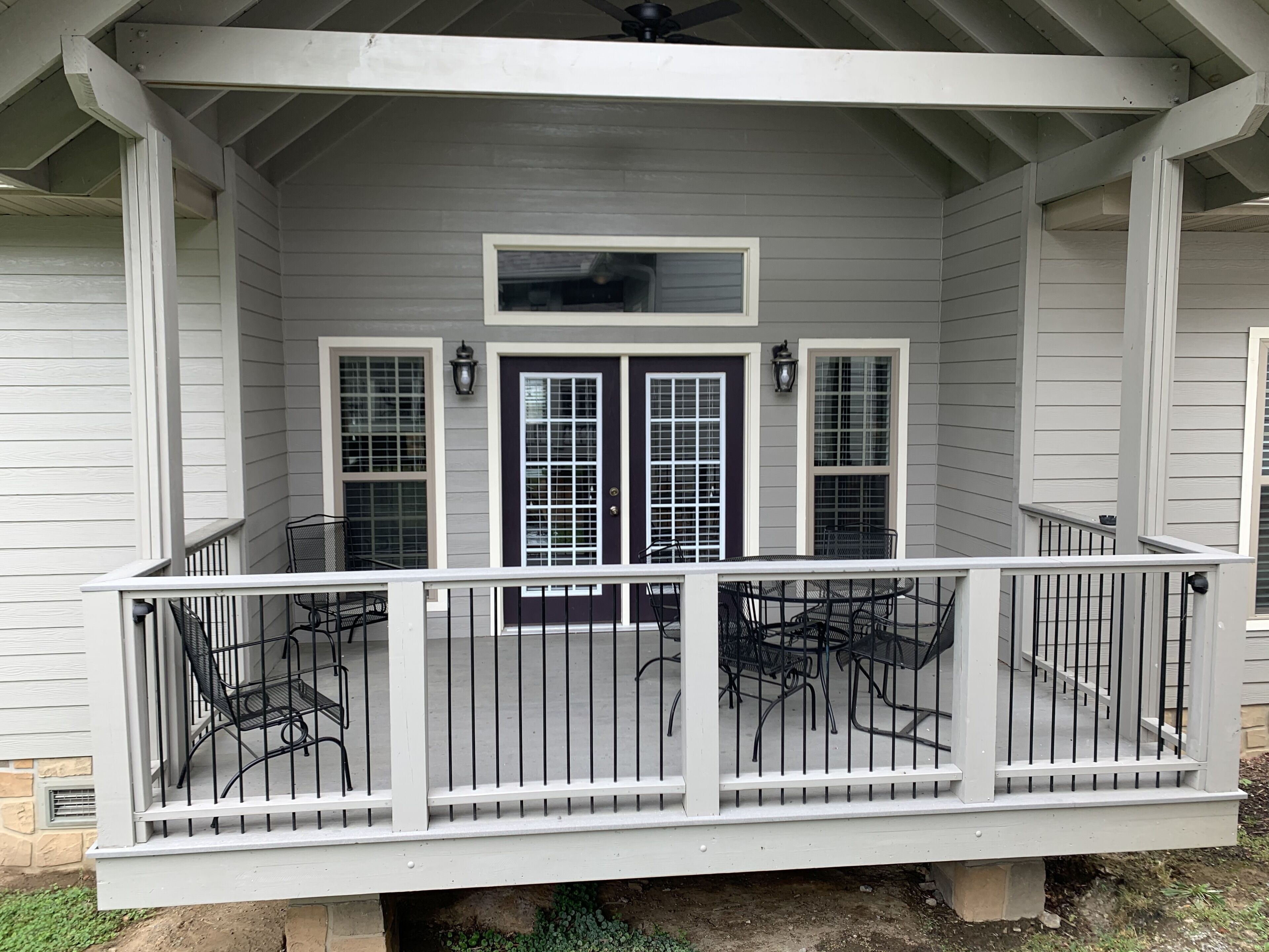 A covered porch with a railing, two doors, and a table with chairs.