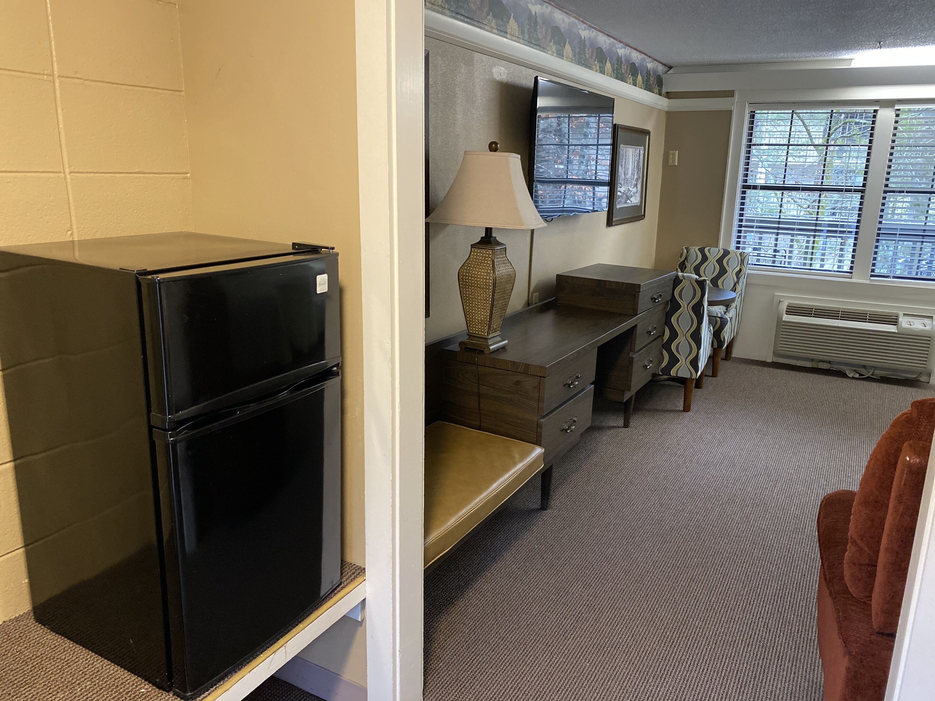 A compact kitchenette with a black refrigerator, a wooden cabinet, a lamp, and a chair.