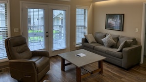 A living room with a brown leather chair, a gray sofa with patterned cushions, a wooden coffee table, and a framed picture on the wall. - Carr's Northside Motel and Cottages (Gatlinburg)