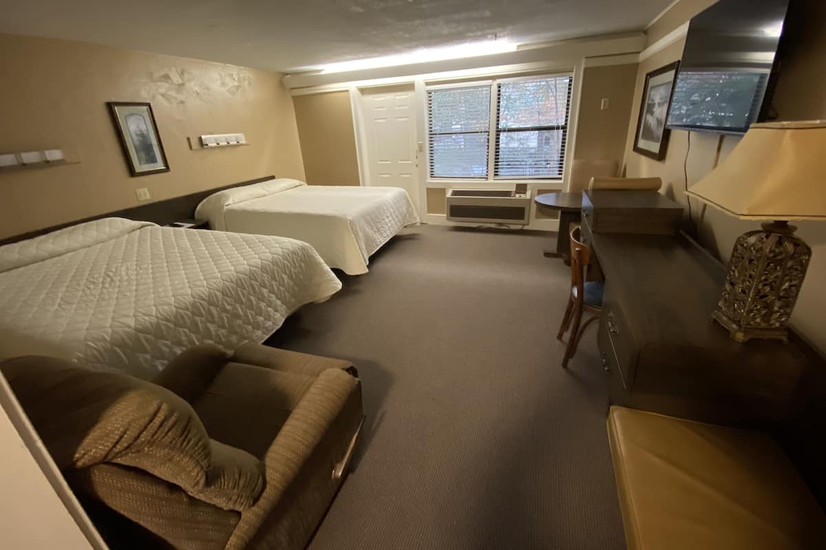 Een hotelkamer met twee eenpersoonsbedden, een bank, een bureau, een stoel, een televisie en een raam met jaloezieën.