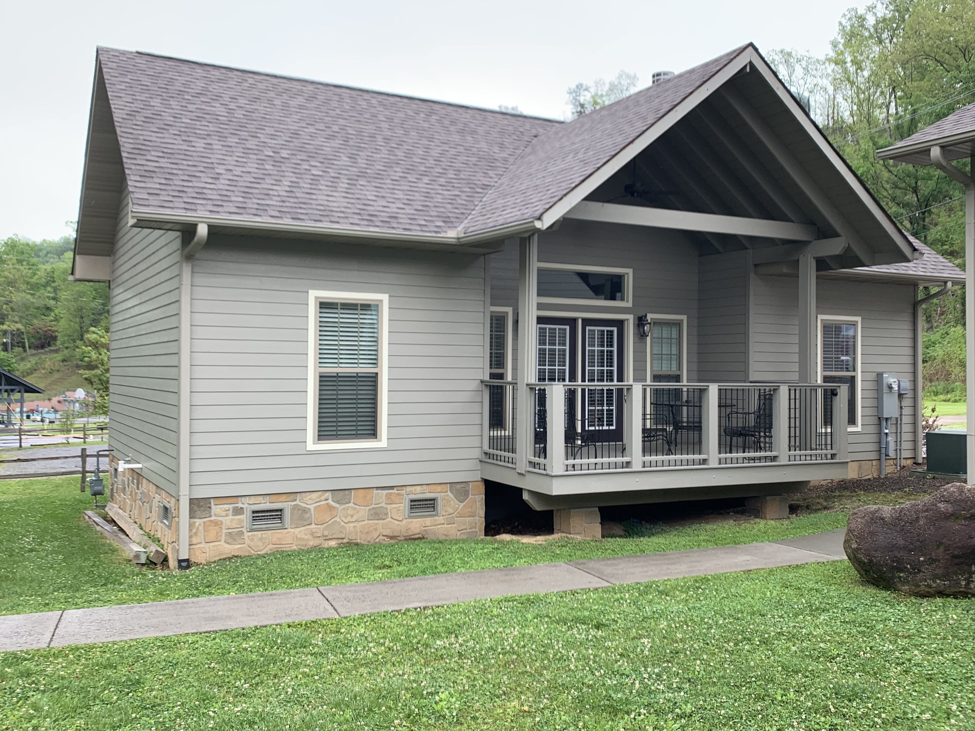 A two-story house with a stone foundation, a covered porch with a railing, and a small front yard.