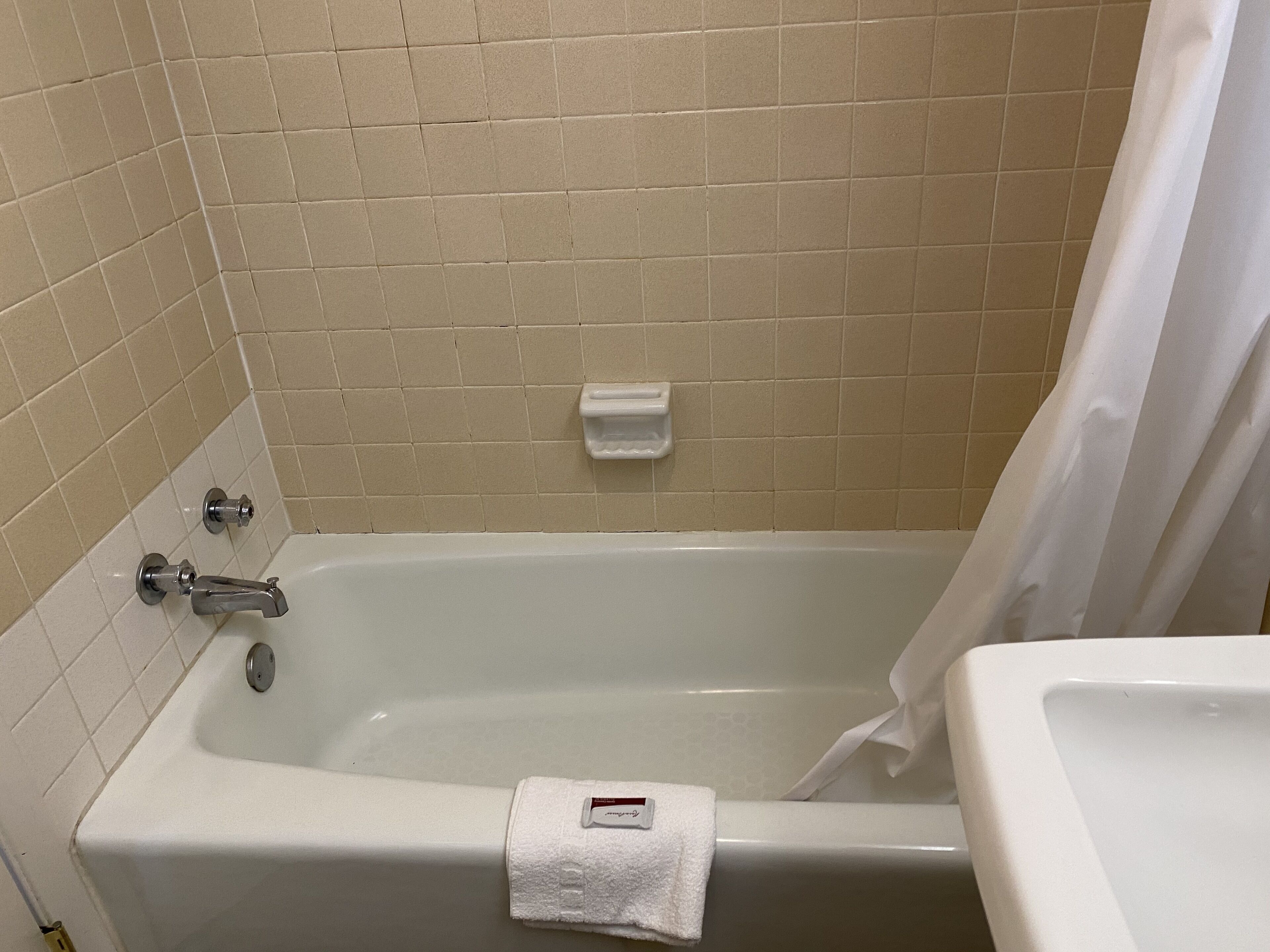 A bathroom with a bathtub, a white towel, and a soap dish on the wall.