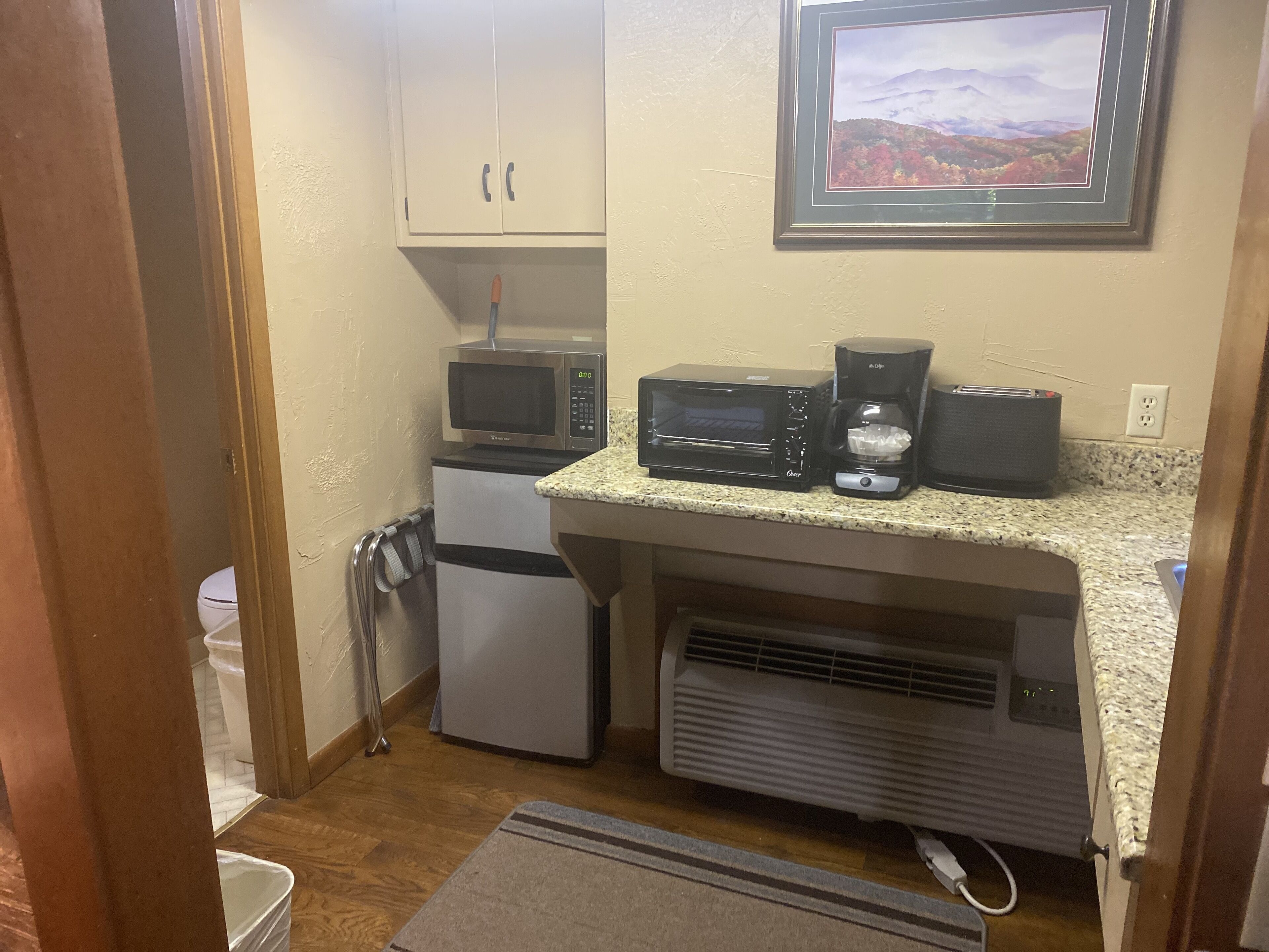 Una kitchenette compacta equipada con microondas, horno tostador, cafetera y un refrigerador pequeño.