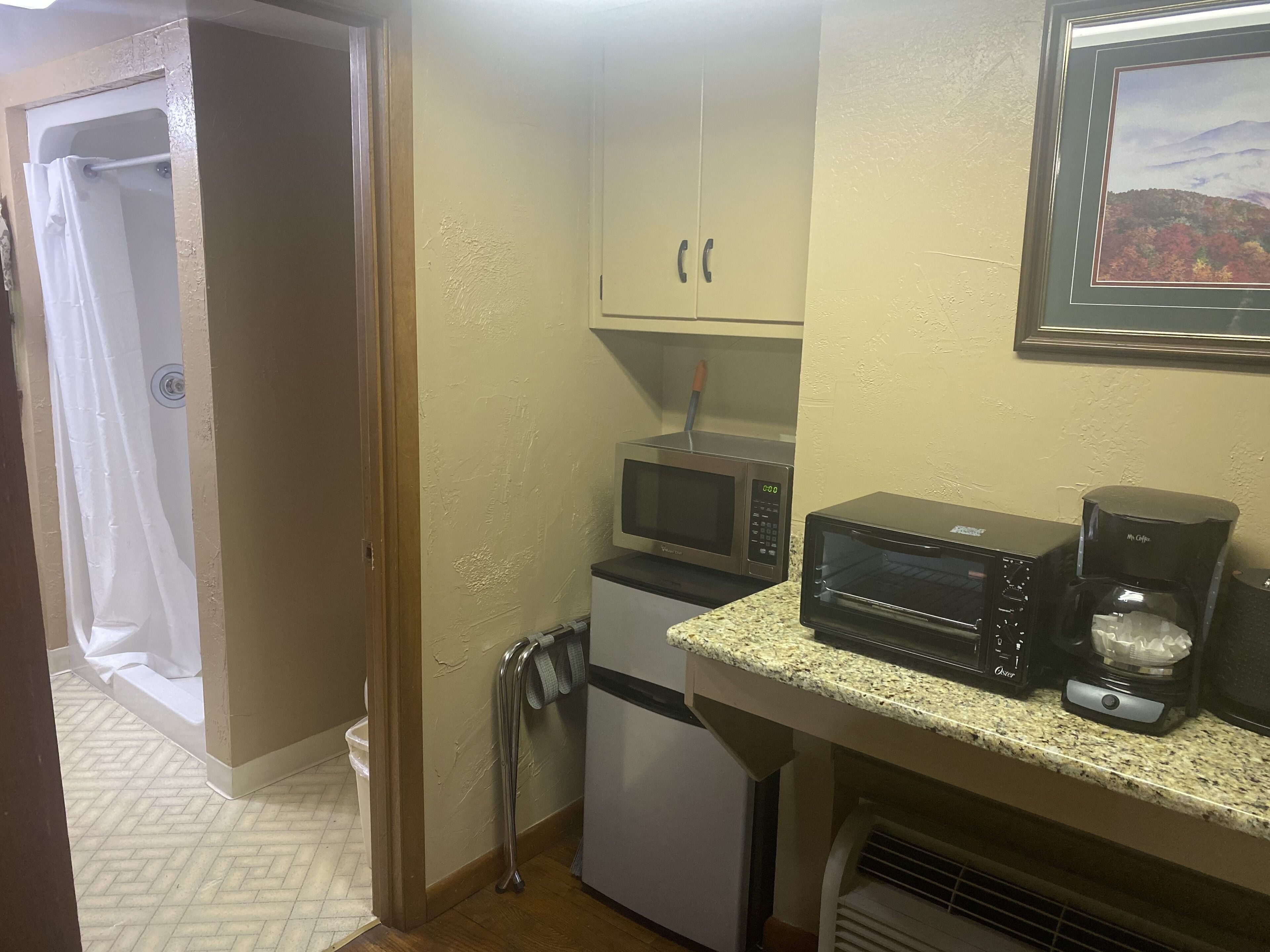 Uma kitchenette compacta com micro-ondas, torradeira e máquina de café sobre bancada de granito.