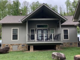 A two-story house with a covered porch, stone foundation, and a stone chimney.