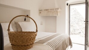 Un dormitorio con una cesta de mimbre sobre la cama, una pared de piedra y vistas a una estructura pétrea exterior.