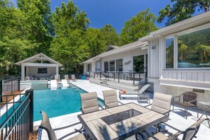 A pool area with lounge chairs, a table, and a covered patio.